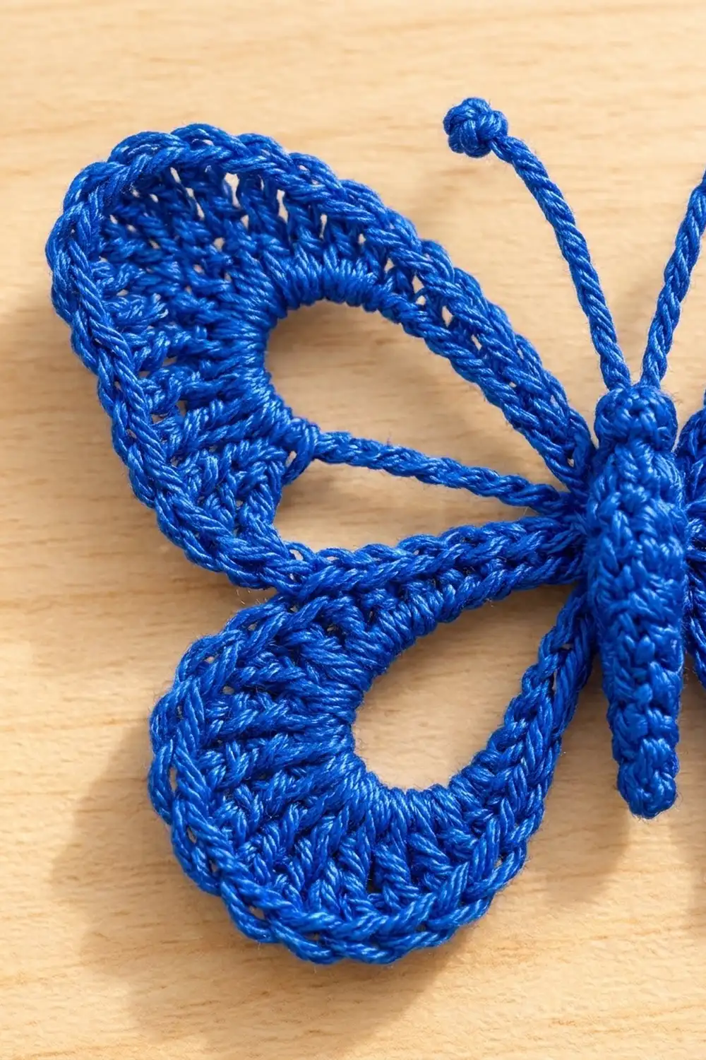 Bright blue crocheted creature with textured stitches and knotted antennae displayed on a natural wood surface.
