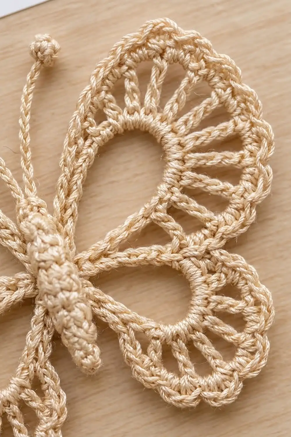 Cream-colored crocheted lace with delicate openwork scallops and detailed stitching on light wood.