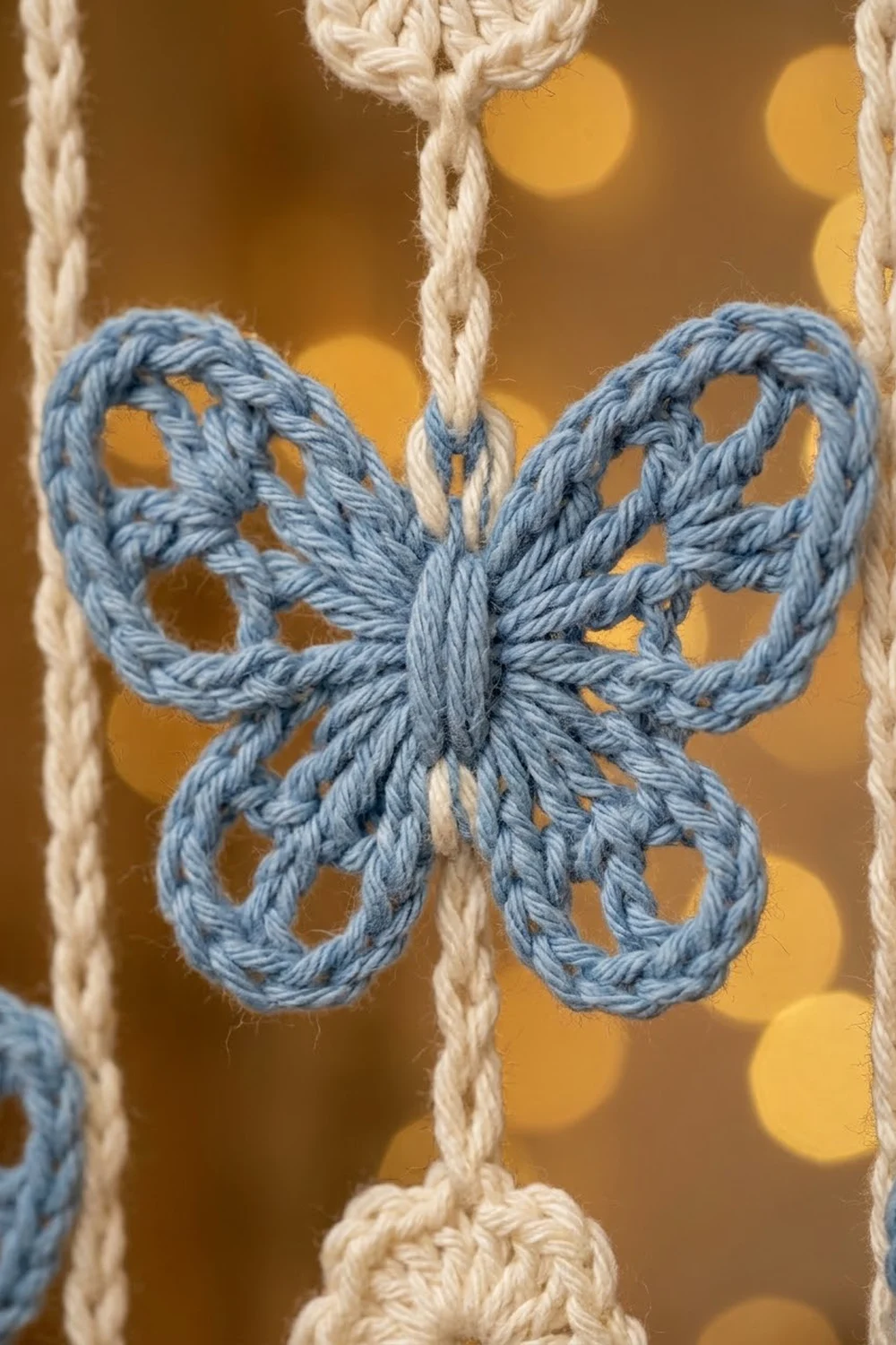A blue rope butterfly ornament hangs from cream-colored twine against a warm, blurred golden bokeh background.