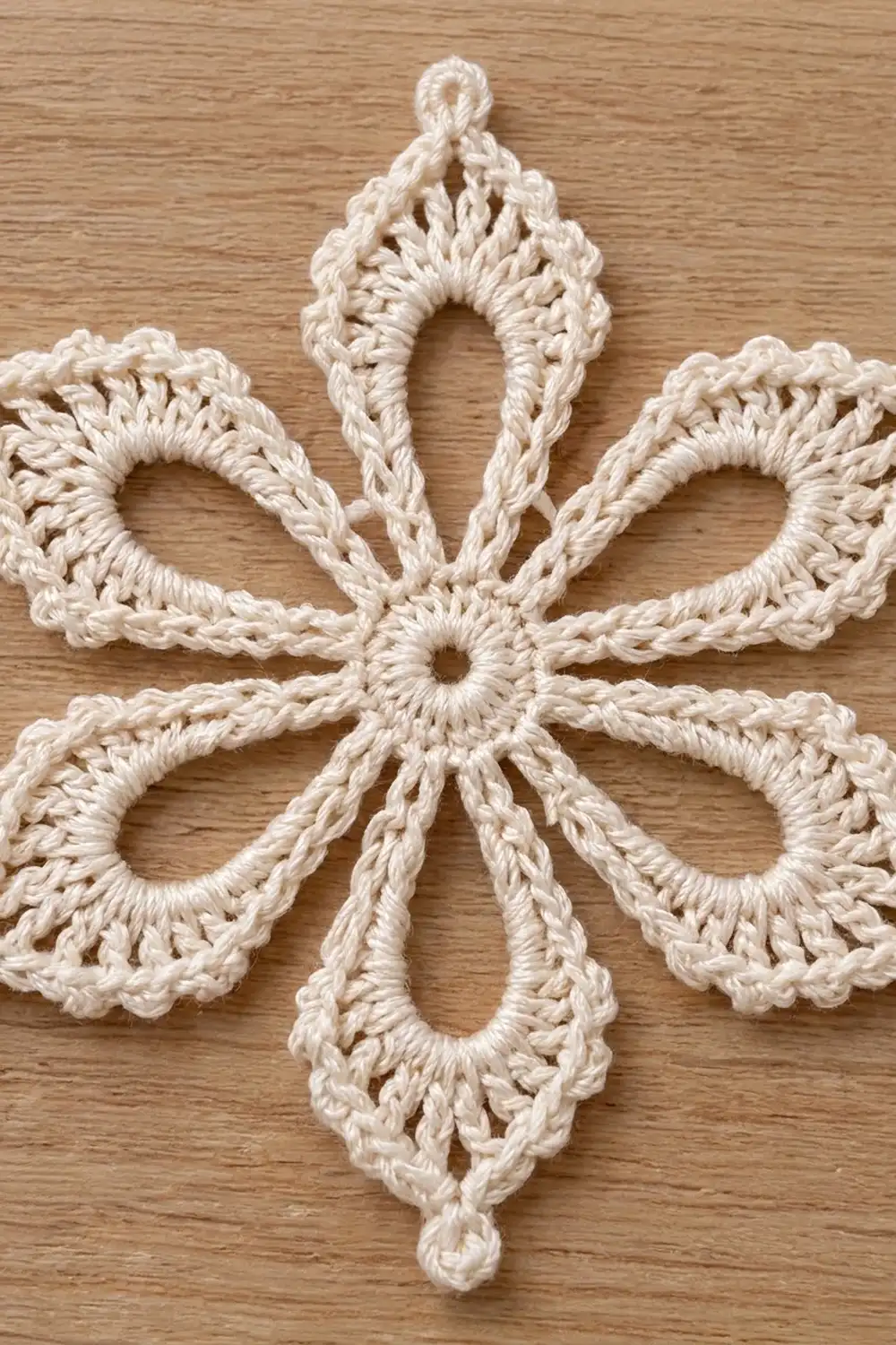 Cream-colored crocheted diamond ornament with delicate four-lobed pattern on warm wooden surface.