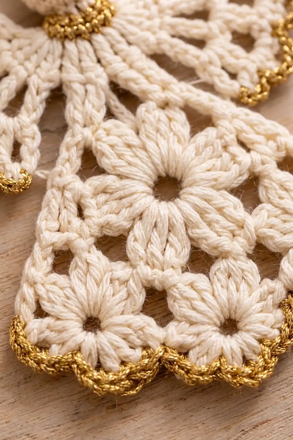 Crocheted cream-colored flower motif with gold trim edging, detailed view on wooden surface.