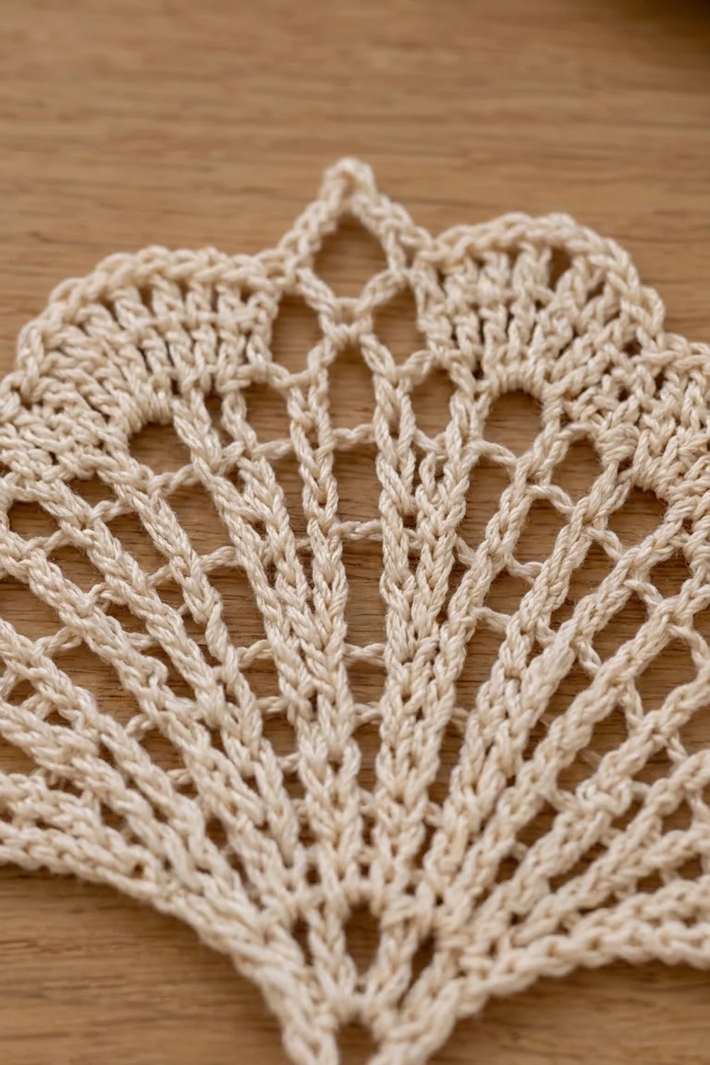 Cream-colored crocheted lace with open stitching in a delicate winged shape on a warm wooden background.