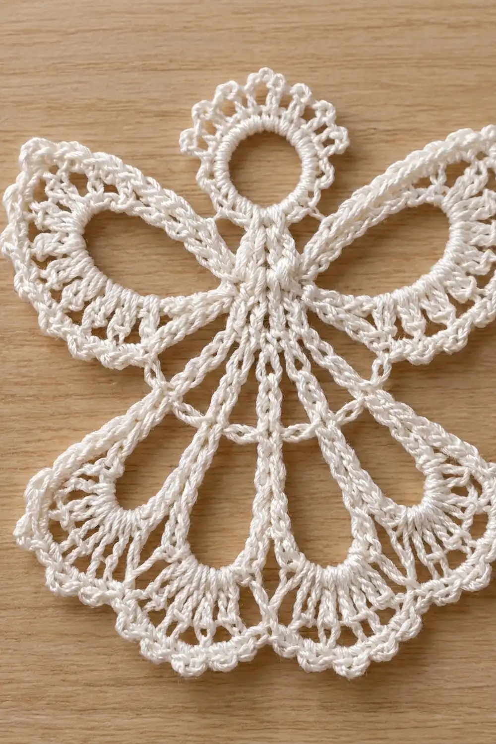 White crocheted snowflake with lobed openwork petals and central ring displayed on warm wooden surface.