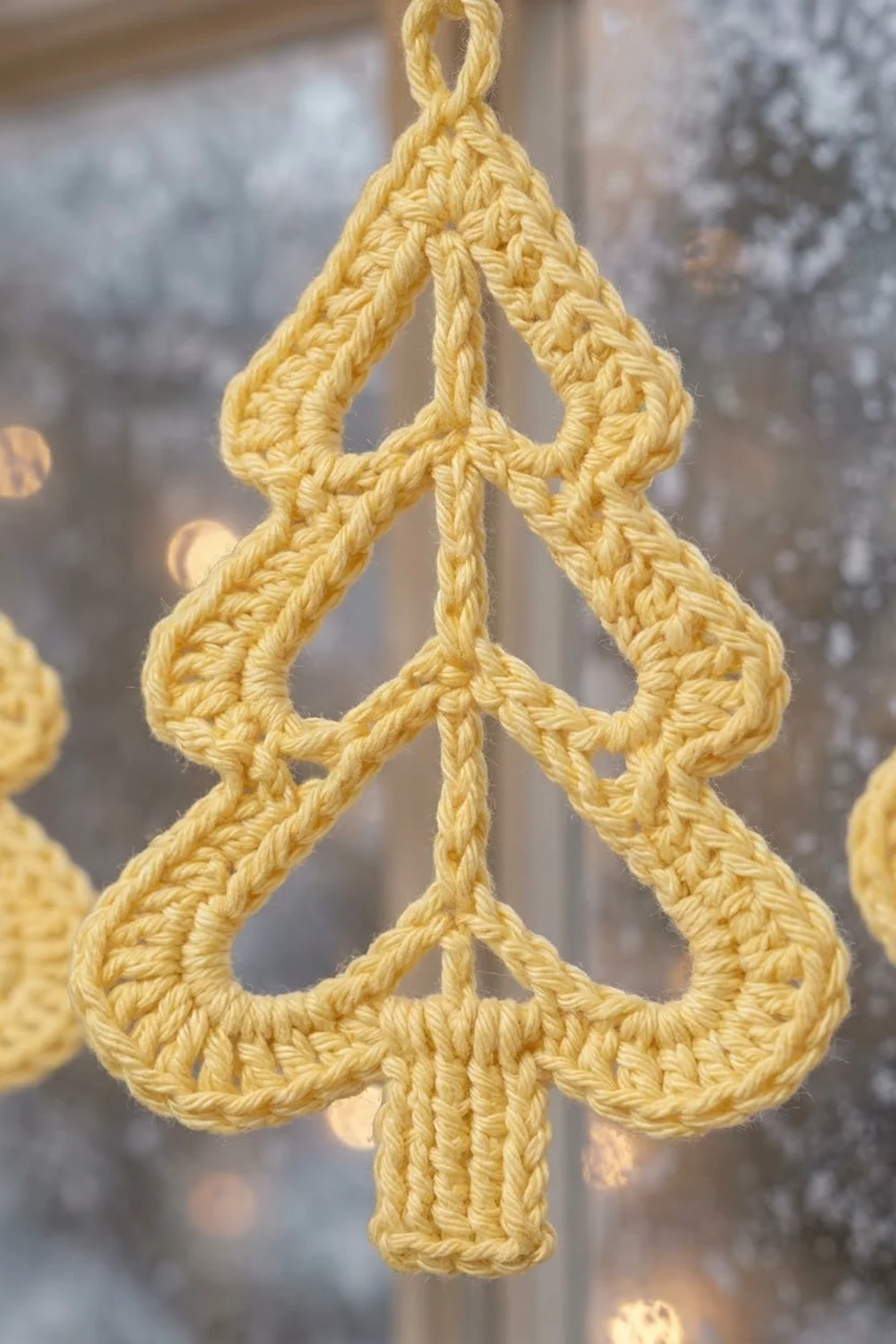 A golden crocheted Christmas tree ornament with decorative loops hanging against a blurred winter background.