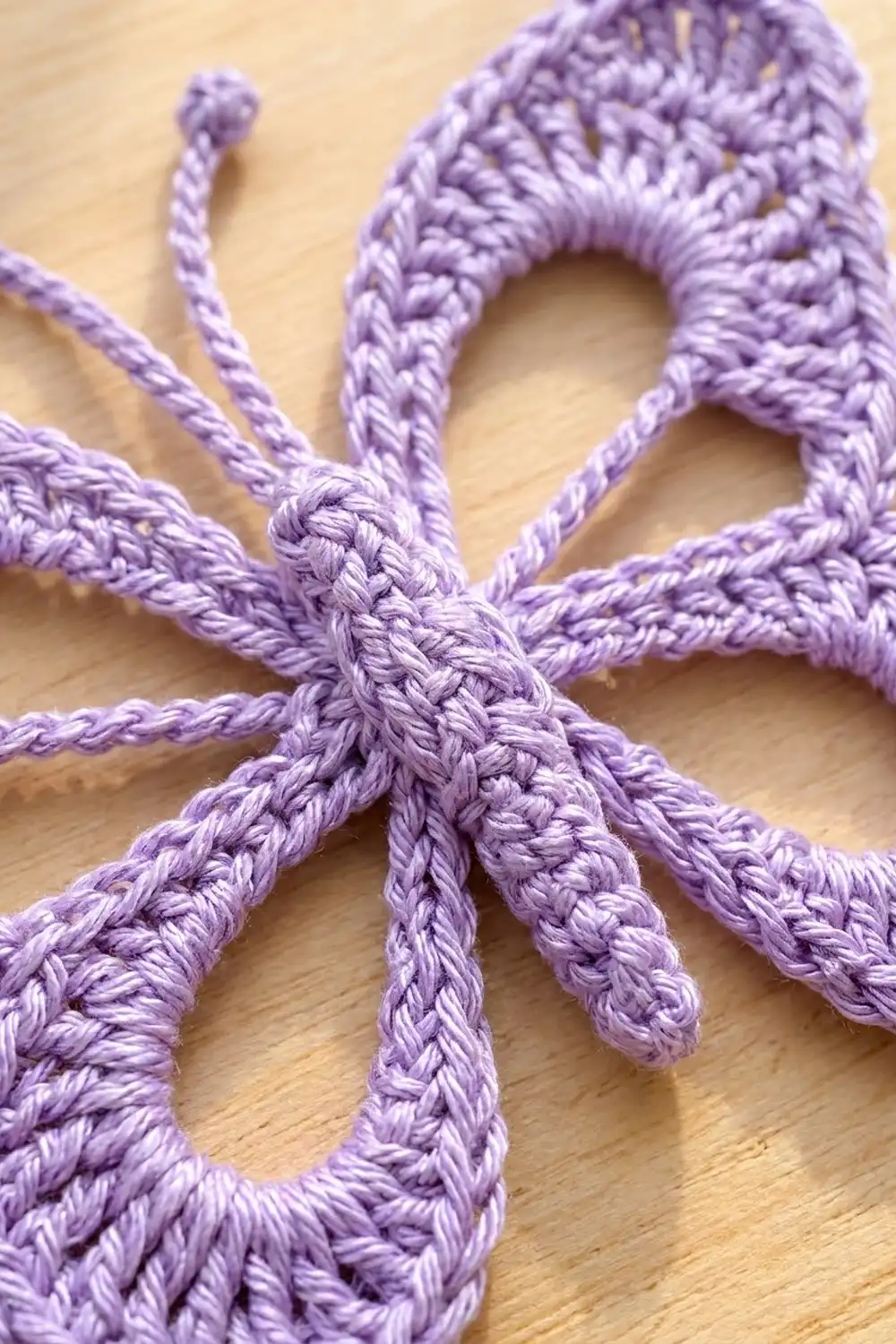 Delicate lavender crocheted motif featuring intricate braided loops and extending strands on a wood surface.