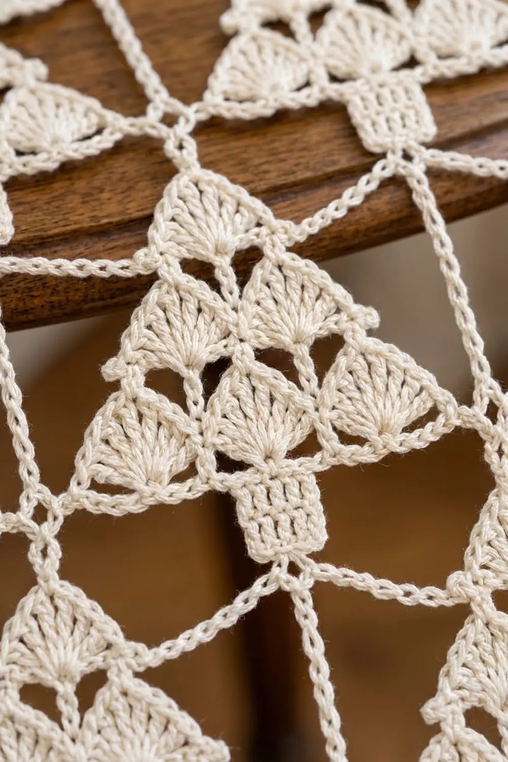 Intricate cream crochet lace with shell stitch pattern displayed on a dark wooden dowel.