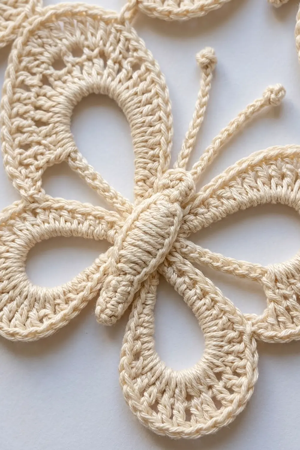 Cream-colored crochet with intricate knotted loops and braided sections photographed against a white background.