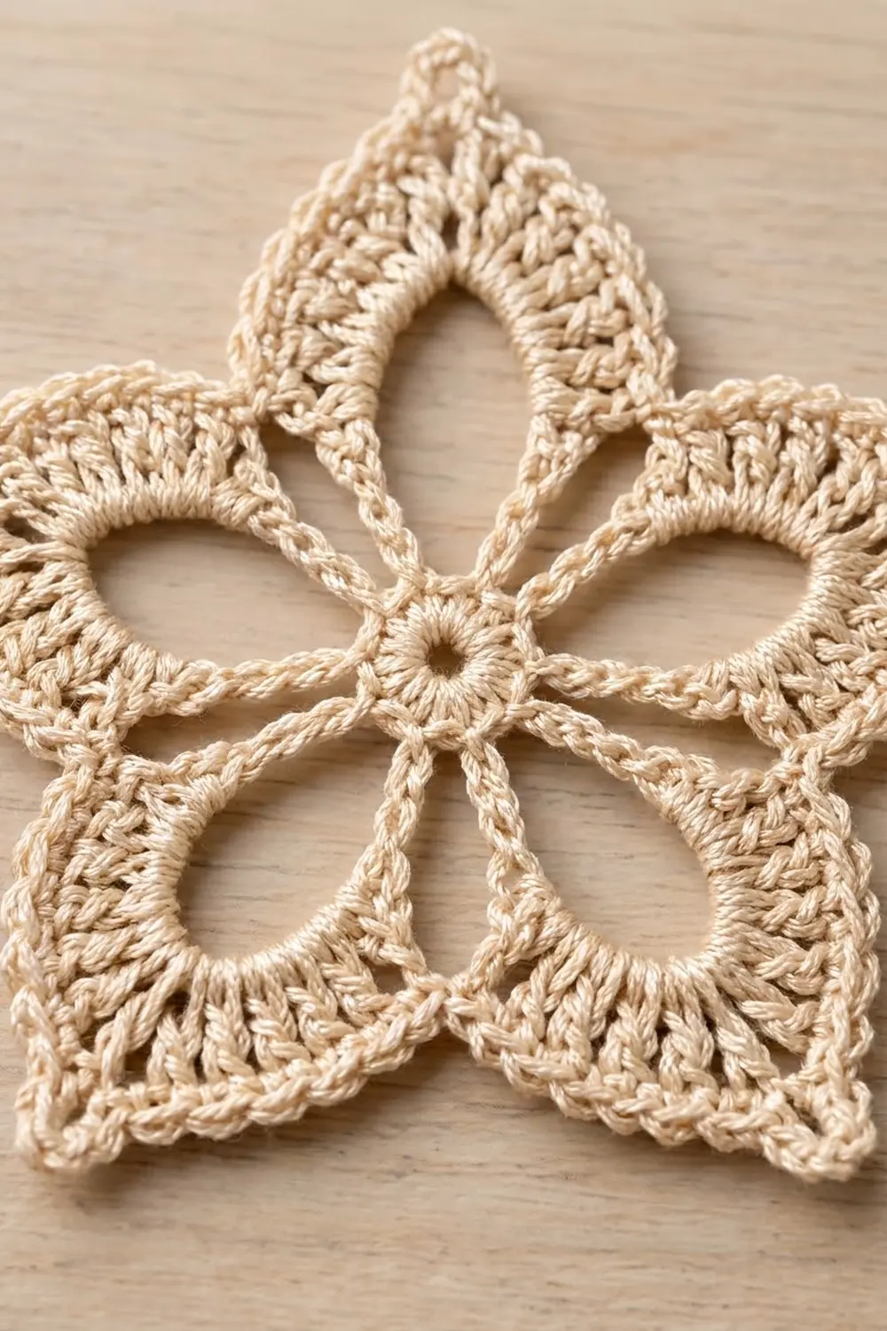 Cream-colored crochet lace with open floral motifs arranged symmetrically on a light wooden surface.