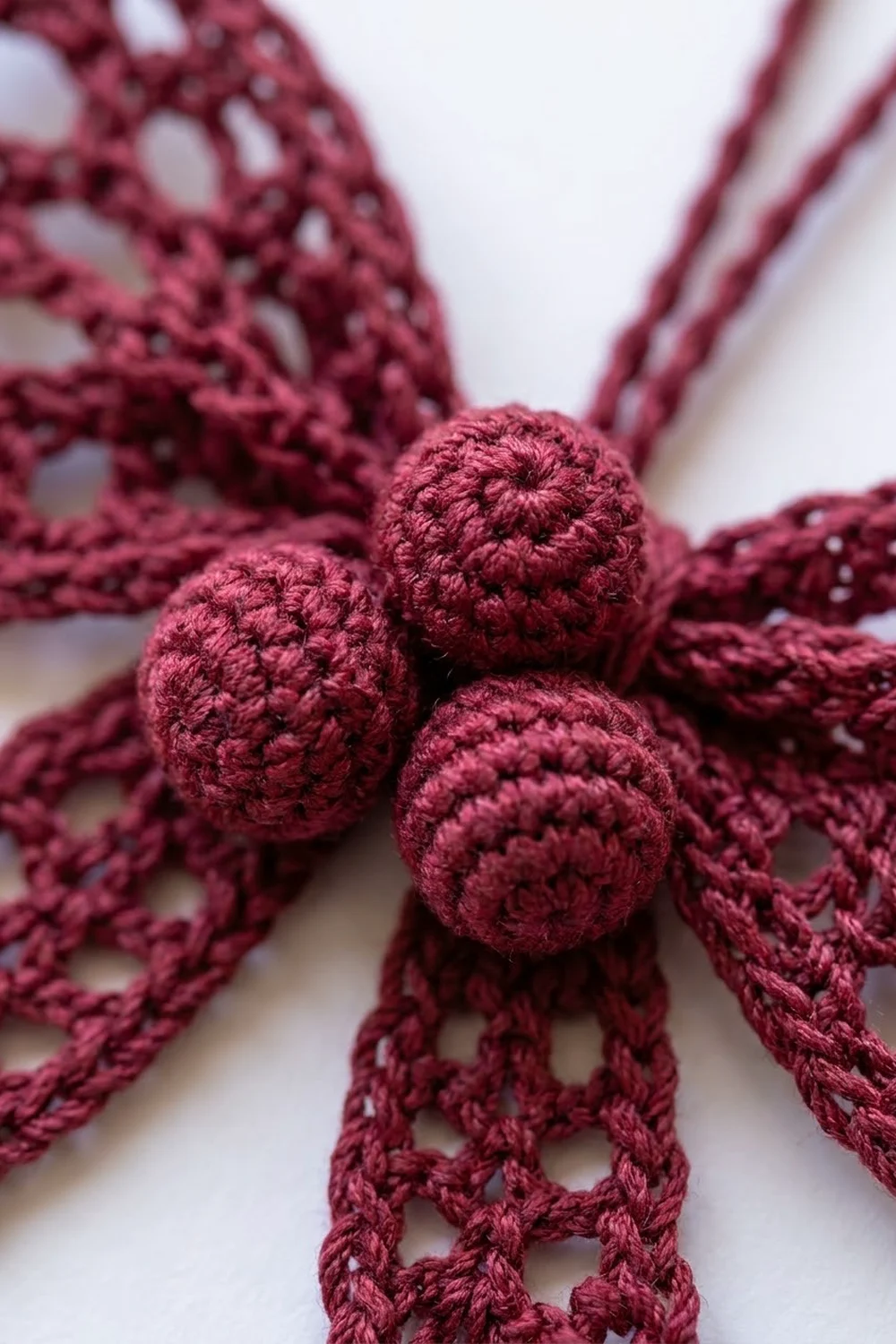 Close-up of three burgundy crocheted balls attached to lacy cords, showing detailed handmade crochet texture on white.
