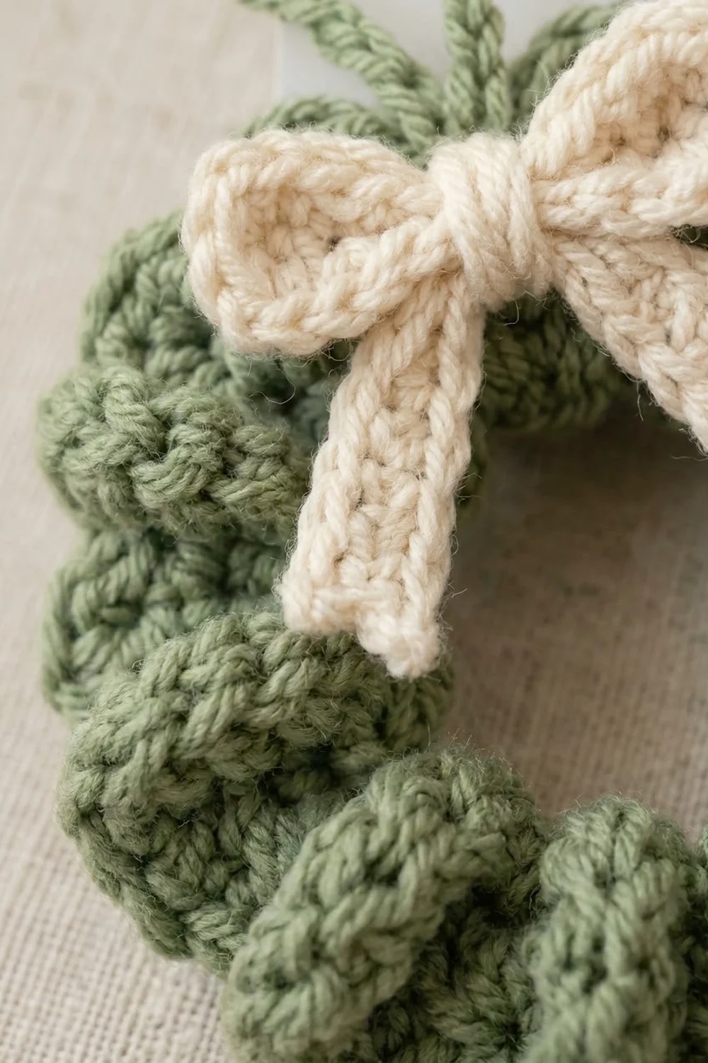 Close-up of a sage green crocheted item tied with a cream-colored braided rope bow.