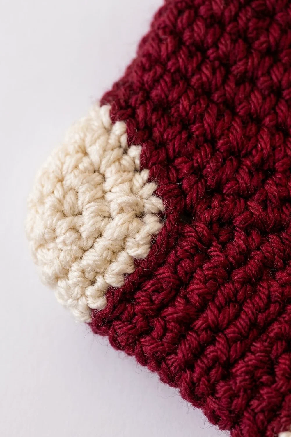 Close-up of crocheted fabric in cream and deep burgundy showing textured stitch detail.