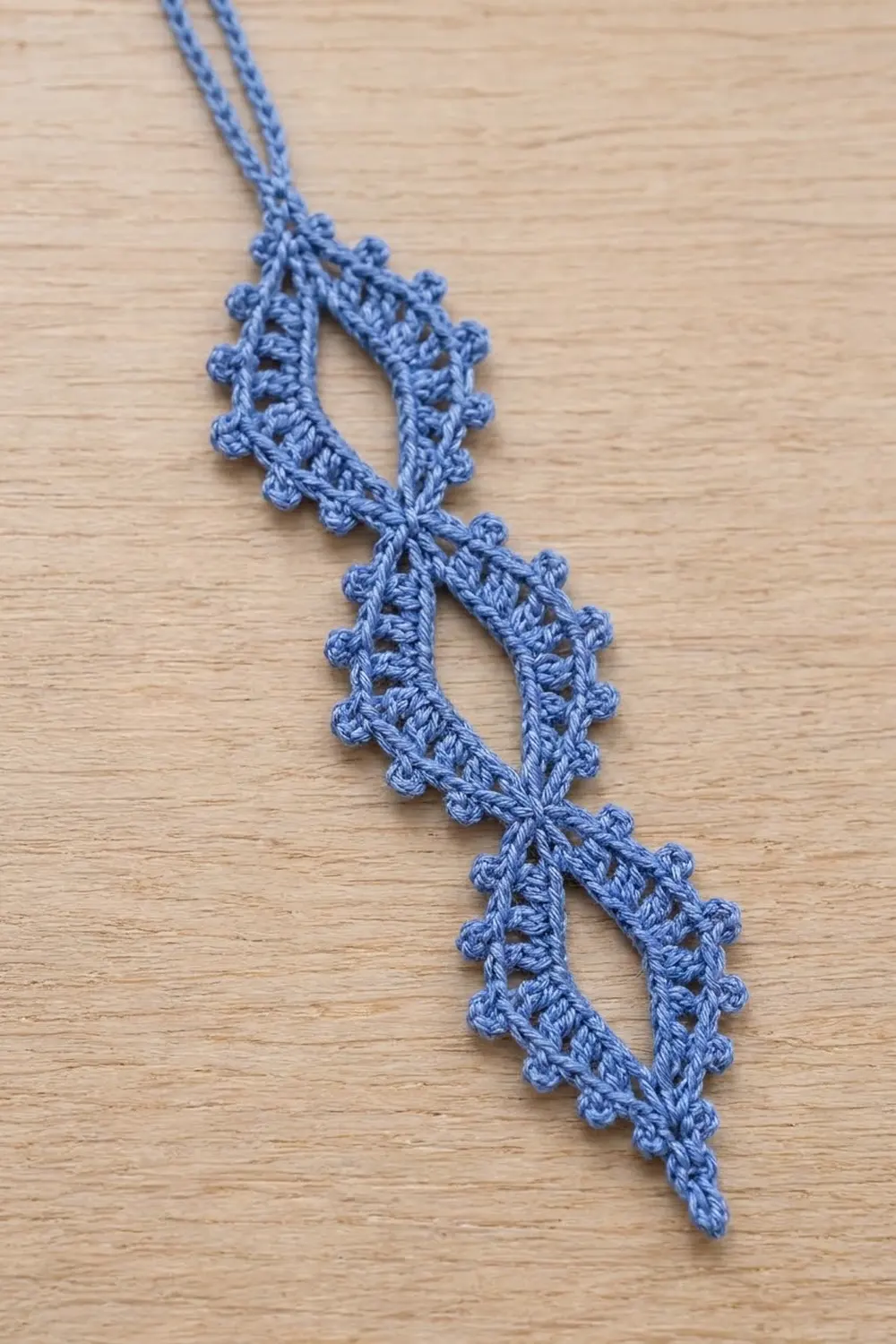 Blue crochet lace trim with delicate picot edging, laid flat on a light wooden surface.
