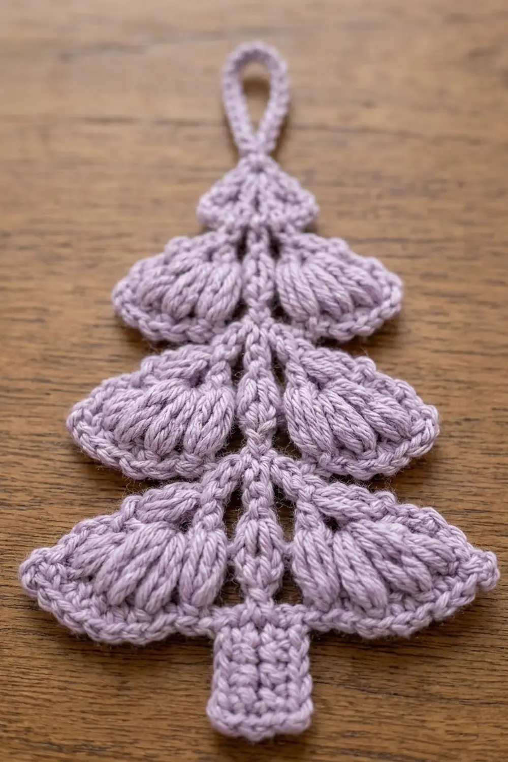 Lavender crocheted Christmas tree ornament with tiered ruffled sections and hanging loop on wooden surface.