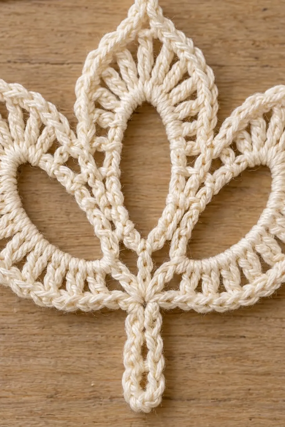 Ornamental cream crochet lace with intricately braided stitches and openwork detail on natural wooden surface.