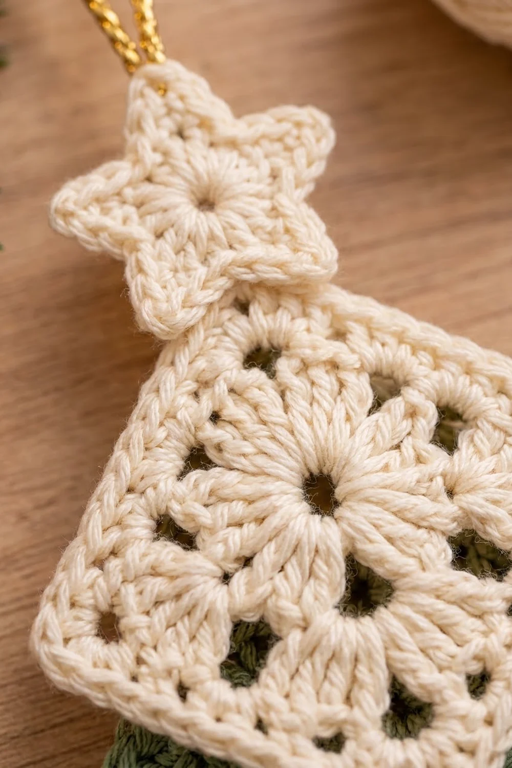 Cream-colored crocheted star ornament with lace-like holes hanging from a gold chain on wood.