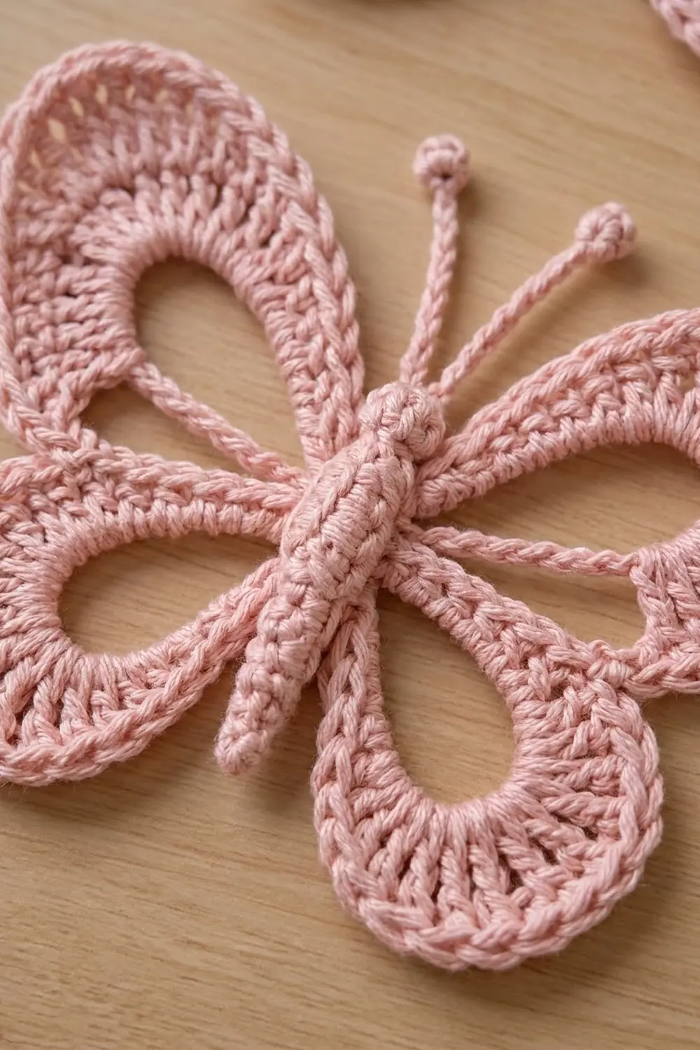 Pink crocheted flower with detailed loop petals and intricate stitches against a light wooden surface.