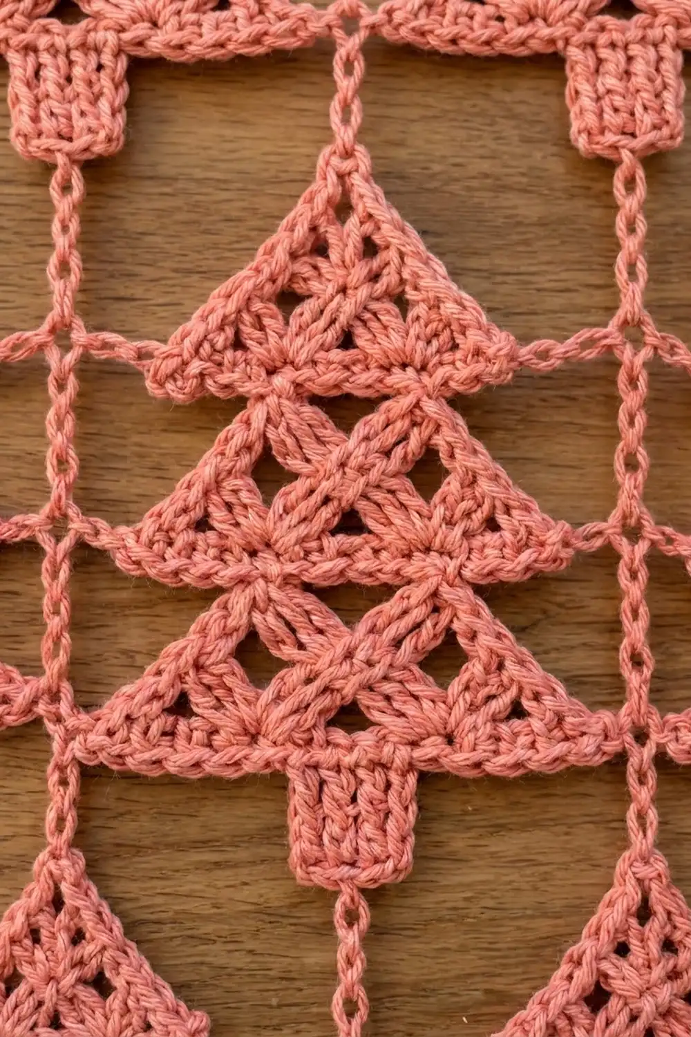Pink crocheted tree ornaments featuring openwork lace patterns displayed on a wooden surface.