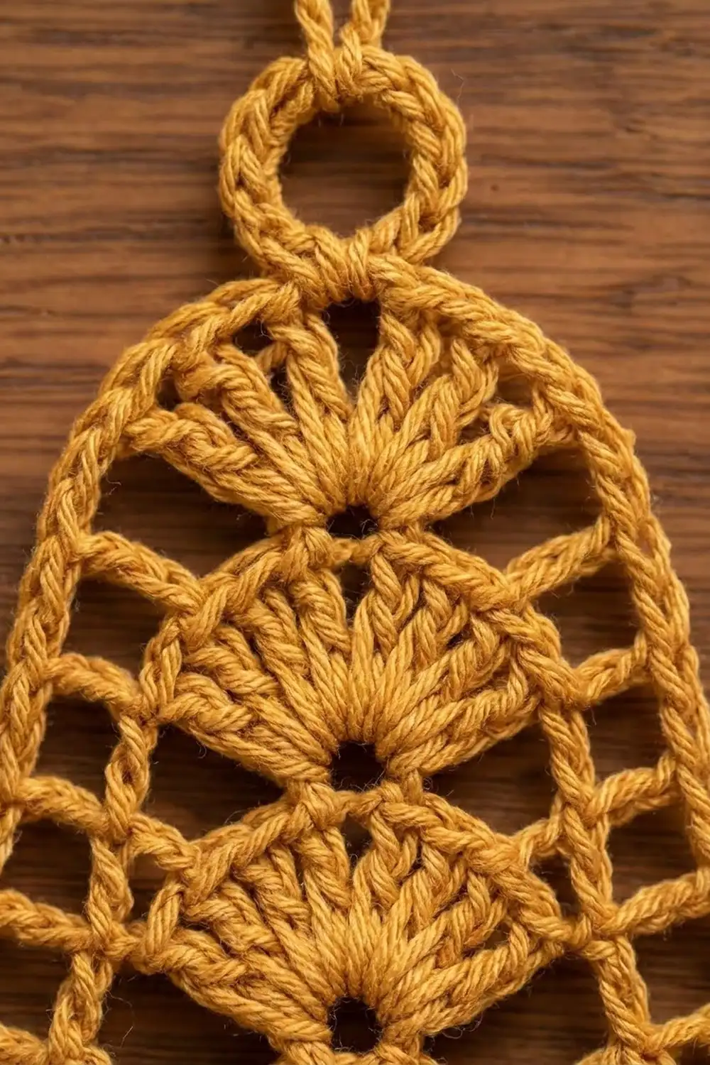 Close-up of a golden yellow macramé wall hanging with knotted flower motifs on wooden background.