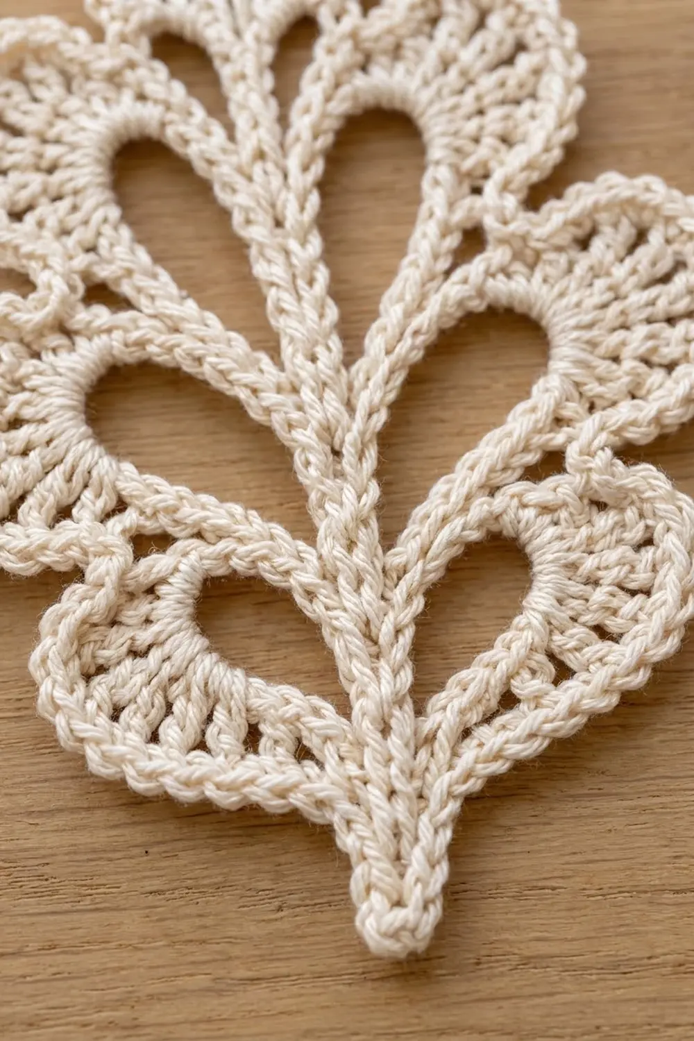 Intricate cream crocheted lace displaying open-work diamond shapes with detailed stitching on a natural wood surface.