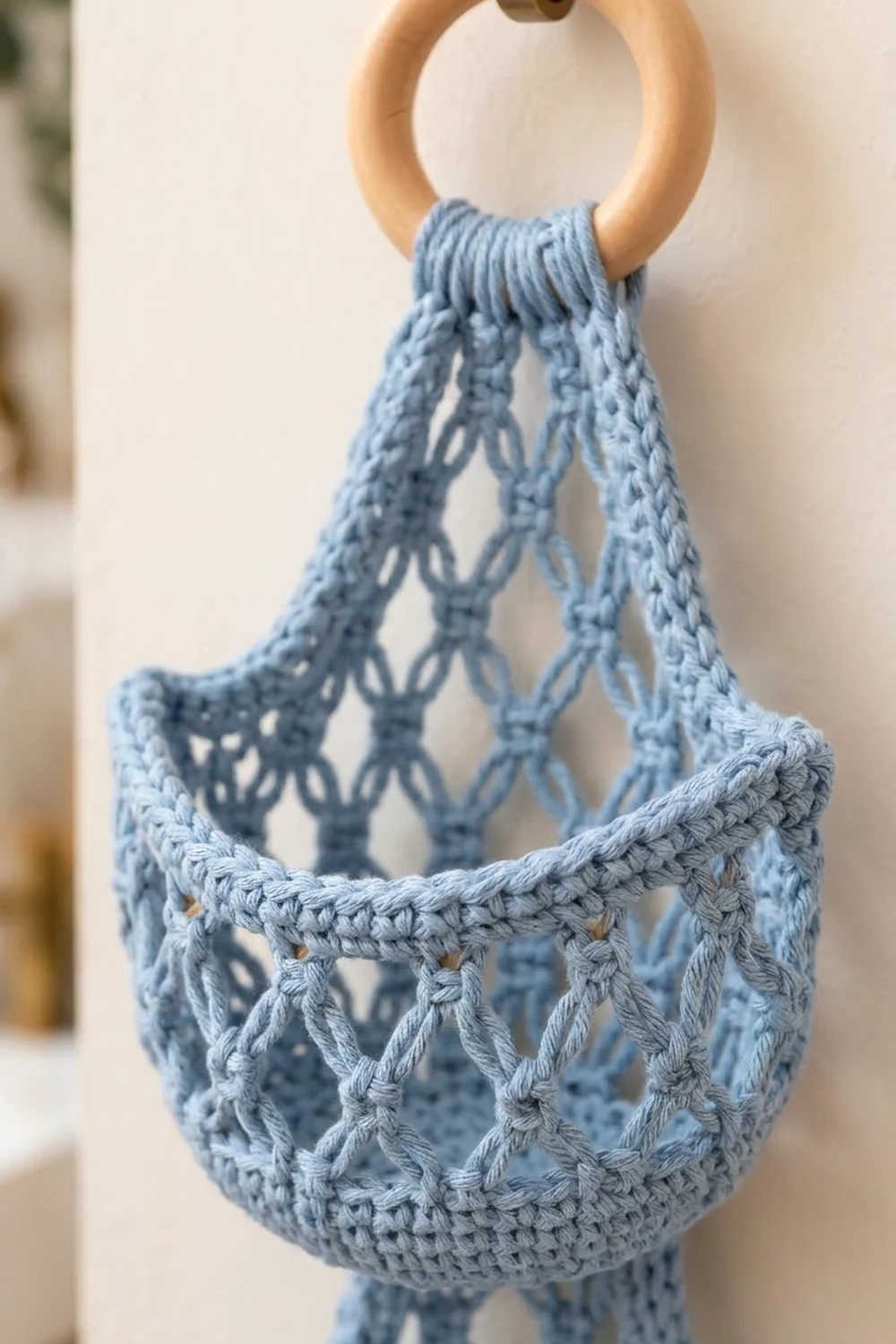 Delicate light blue crocheted mesh bag with intricate openwork pattern suspended from wooden ring handles.