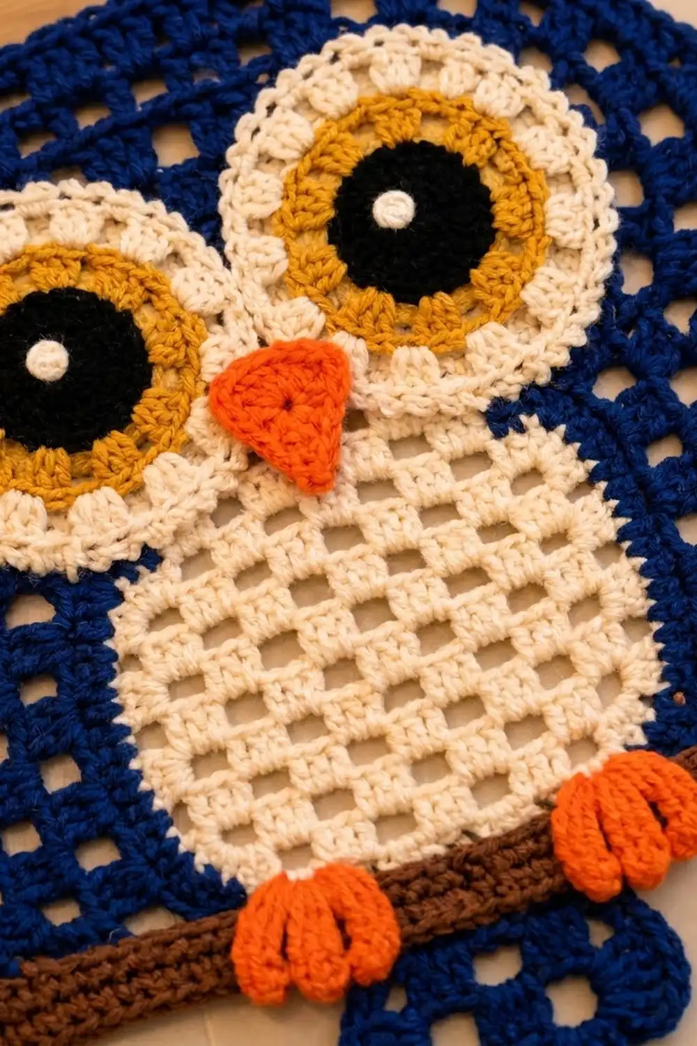 Crocheted owl with golden eyes, orange beak, and detailed navy-blue and cream yarn stitching.