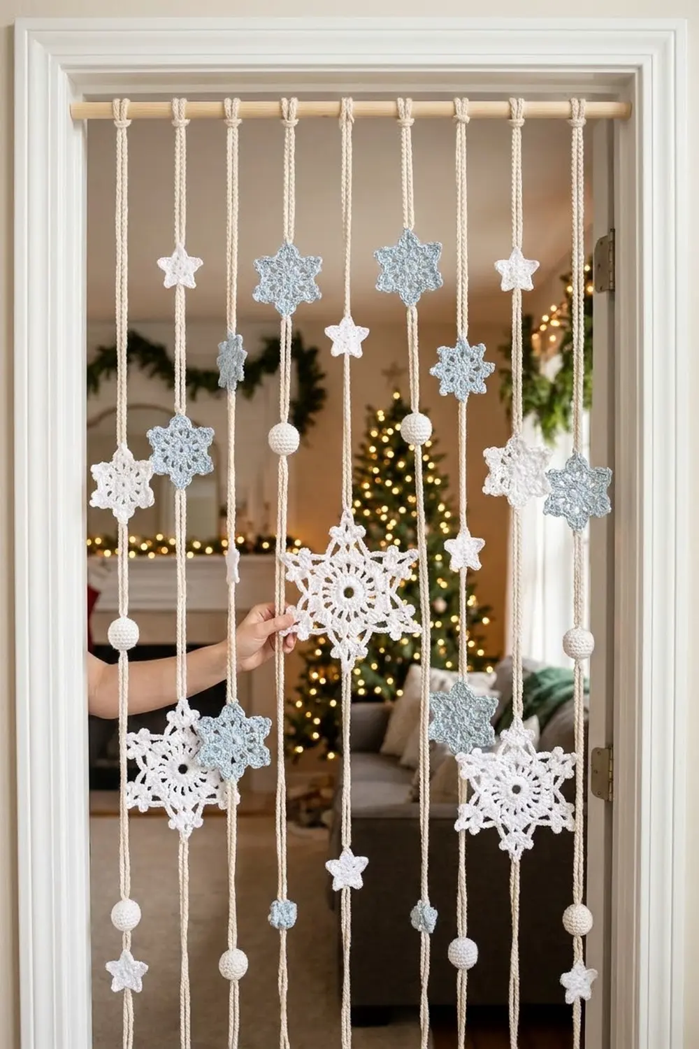 White and blue crocheted snowflakes and beads hanging from a wooden rod spanning a window with holiday lights beyond.