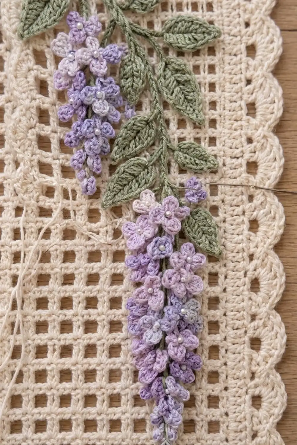 Crocheted purple lilac flowers with green leaves stitched on cream lace crochet fabric on a wooden table.