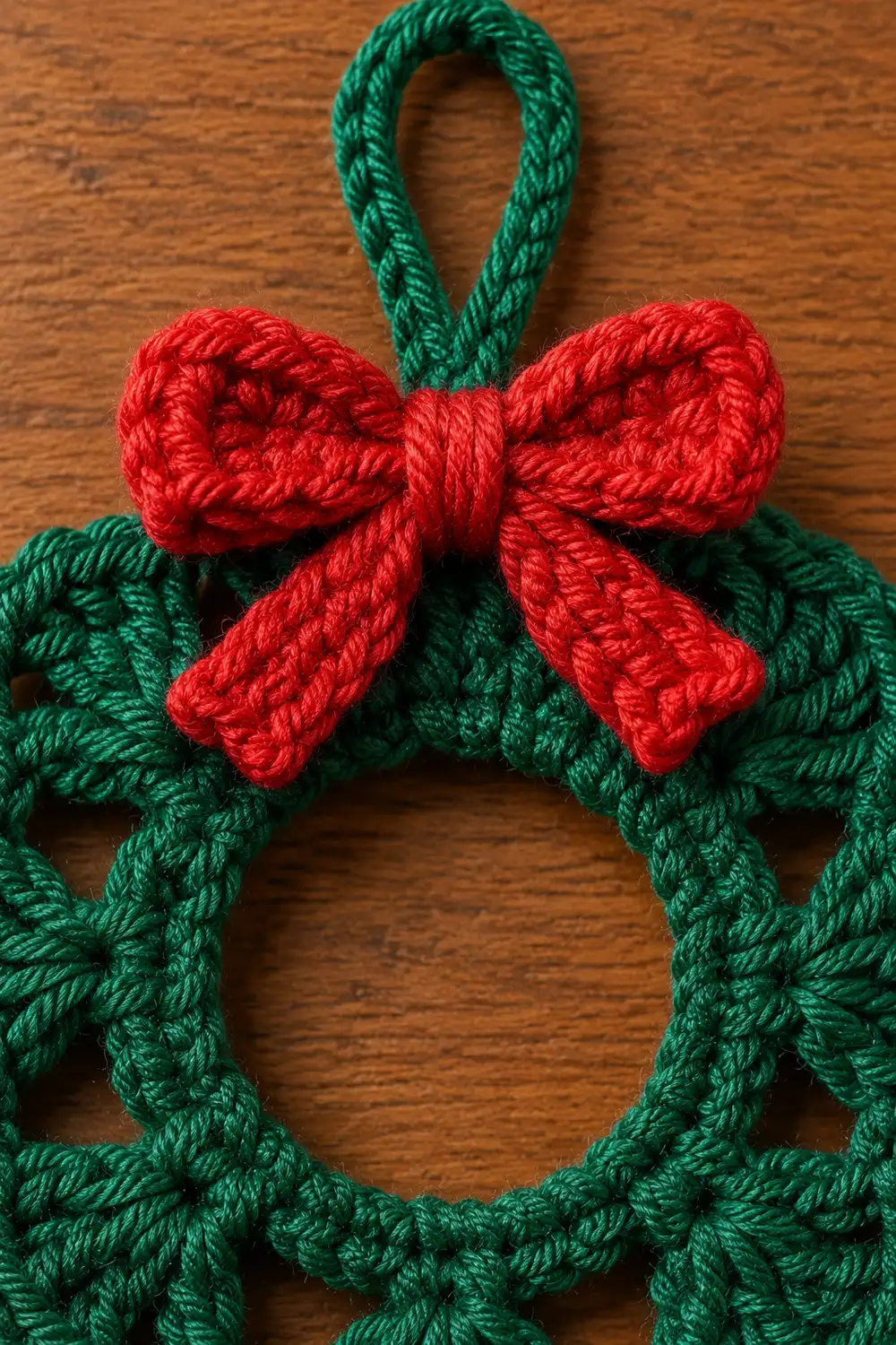 A handmade crocheted wreath with green rope and red bow ornament on a wooden surface.