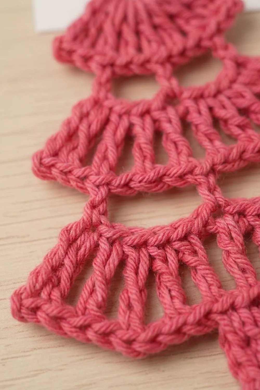 Close-up of pink crocheted lace trim with shell stitch pattern displayed on a light wood surface.