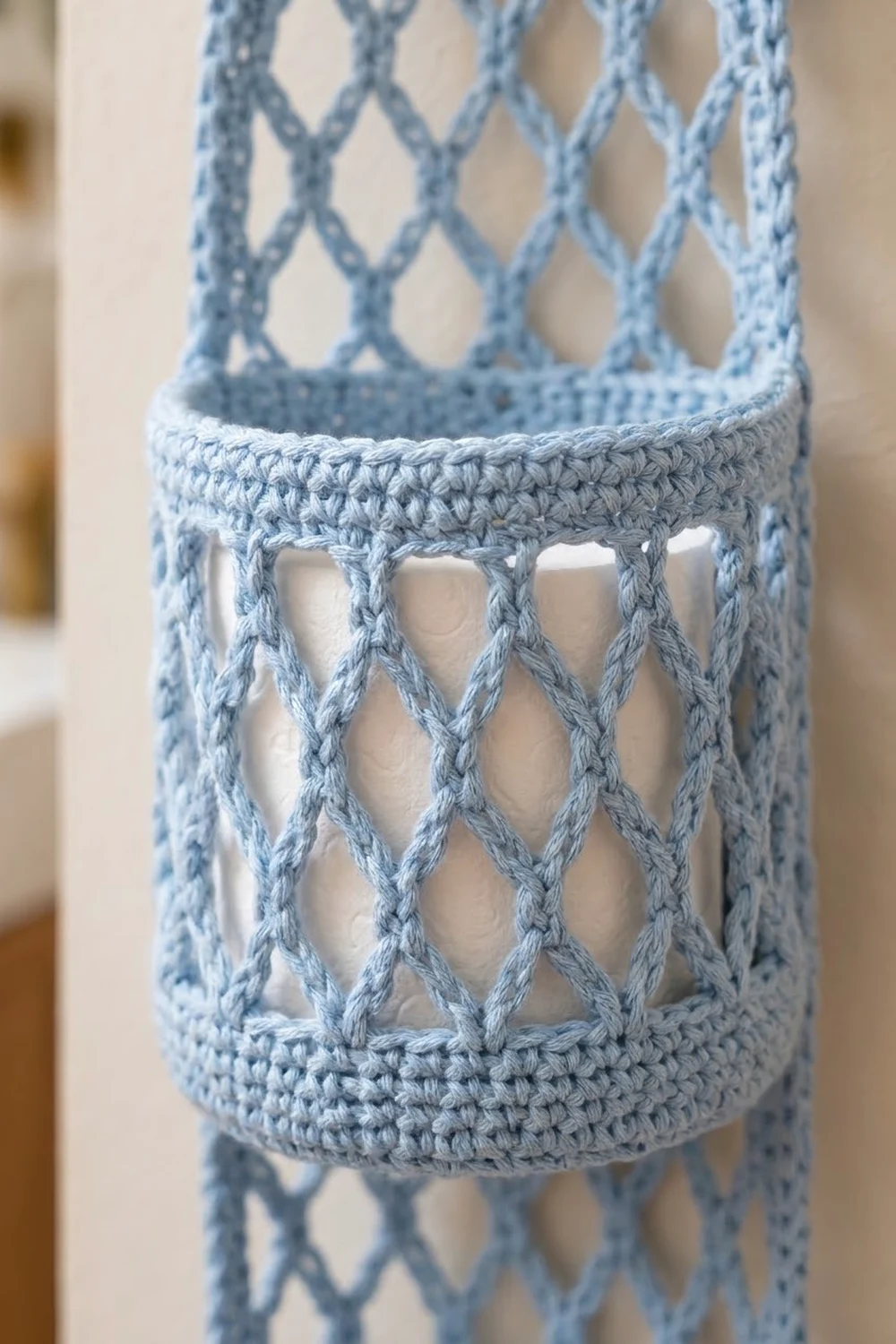 Close-up of a light blue crocheted tube with an open lattice diamond pattern and solid ribbed bands.
