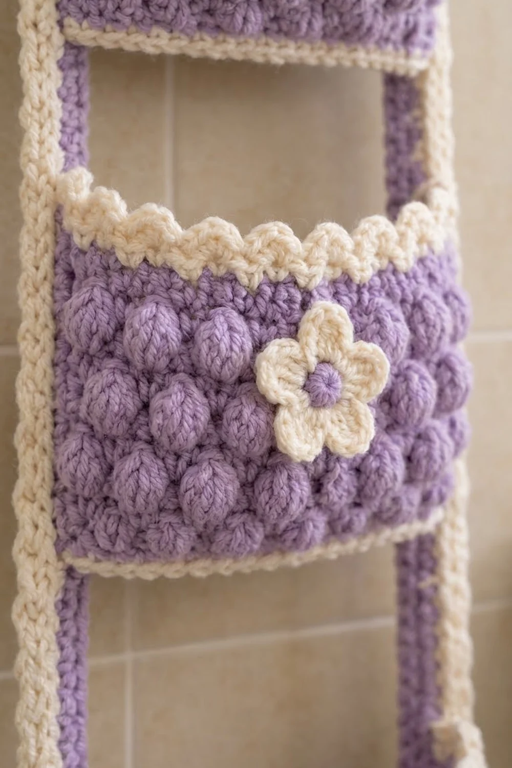 A lavender crocheted bag features textured popcorn stitches, cream borders, and a cream flower with lavender center.