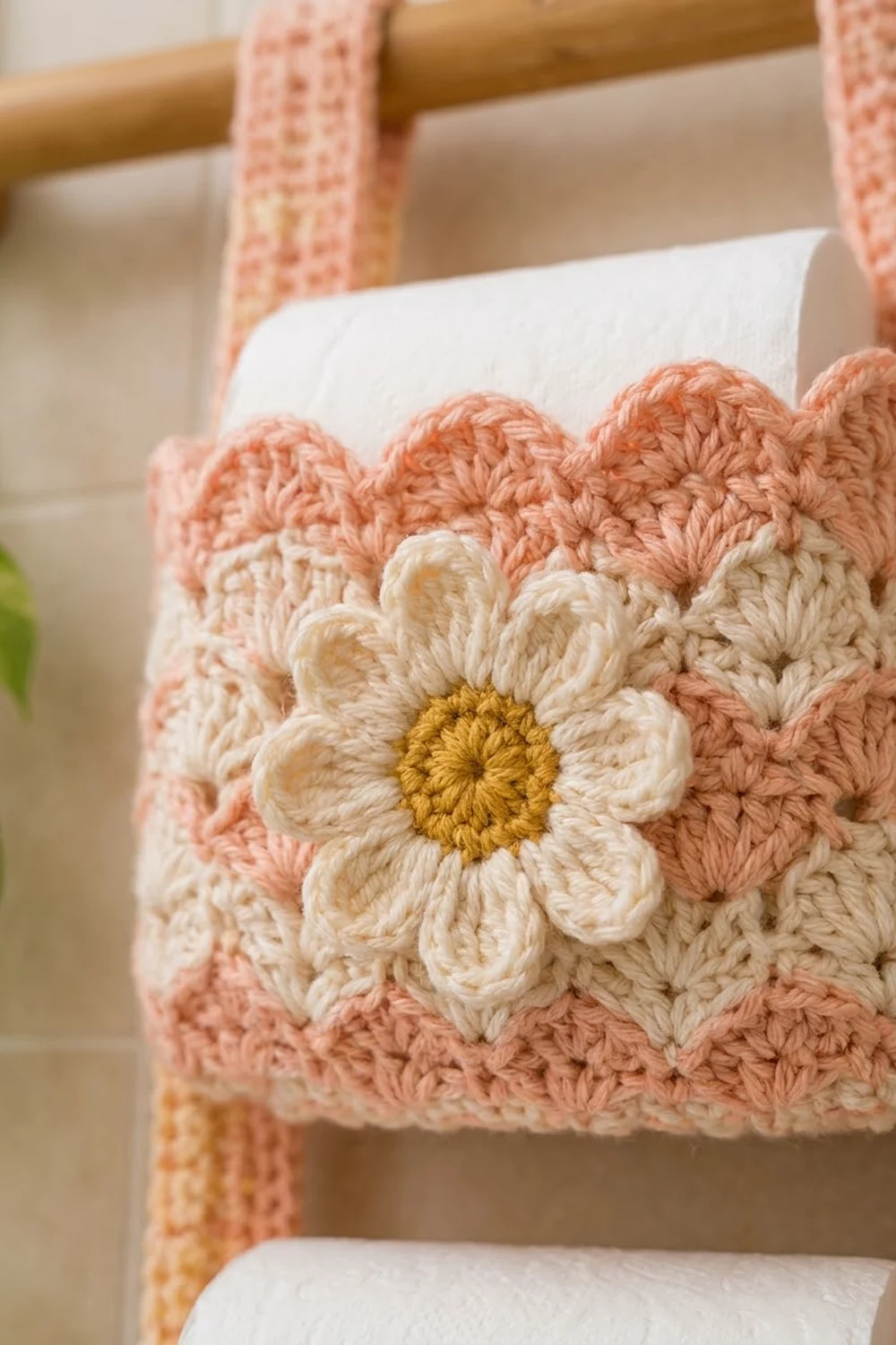Crocheted white daisy with golden center on a peachy-pink cushion resting on a wooden chair.