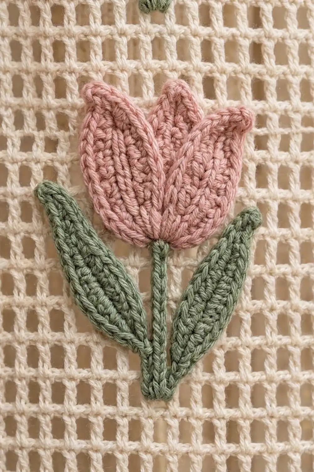 Pink crocheted tulip with green leaves appliquéd on a cream-colored waffle knit fabric.