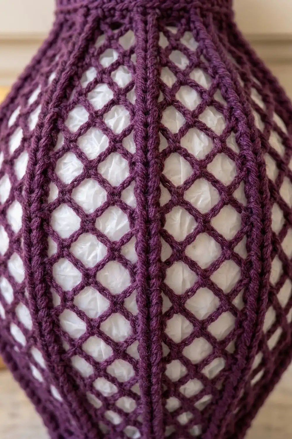 Detailed view of deep purple crocheted lace featuring diamond-shaped openings and raised stitches against a warm background.