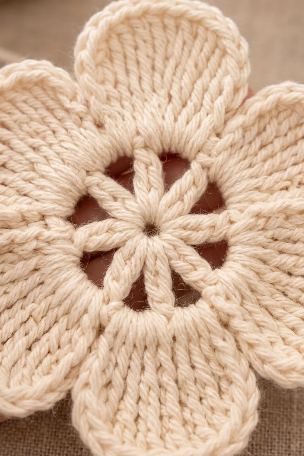 Close-up of cream-colored rope knotwork forming an intricate flower-like pattern with geometric openings against a soft, blurred tan background.