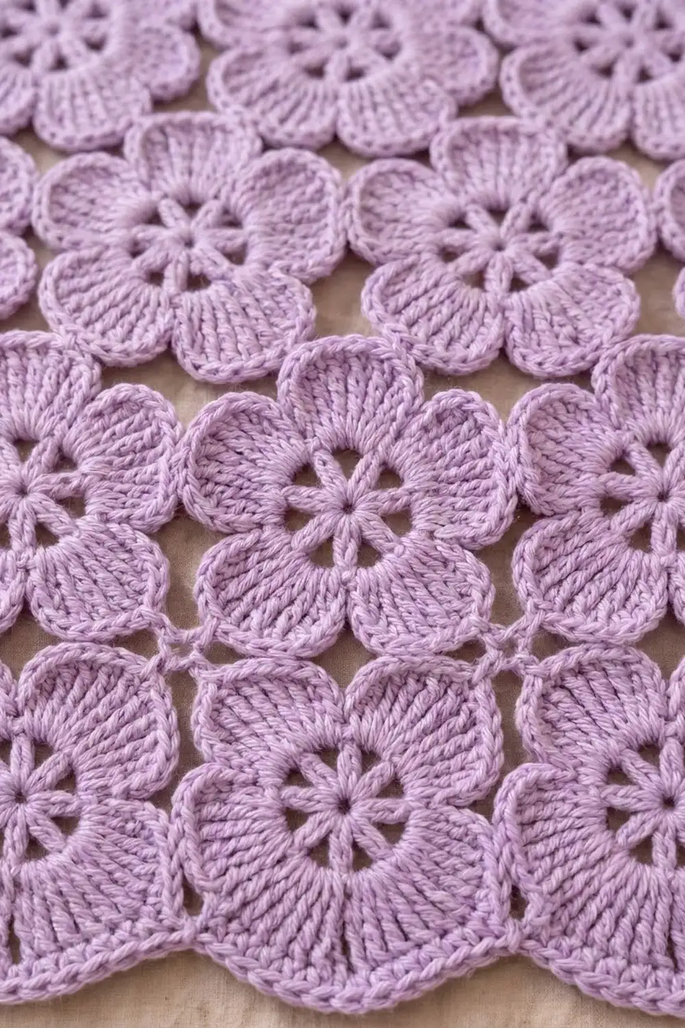 Close-up of delicate lavender crocheted flower motifs with openwork petals arranged on a cream-colored background.