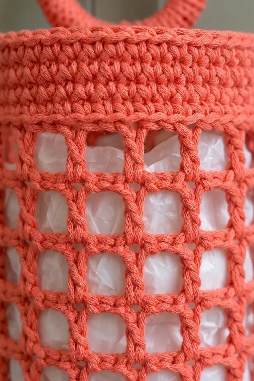 Coral-pink crocheted mesh fabric with open square lattice pattern and textured yarn detail.