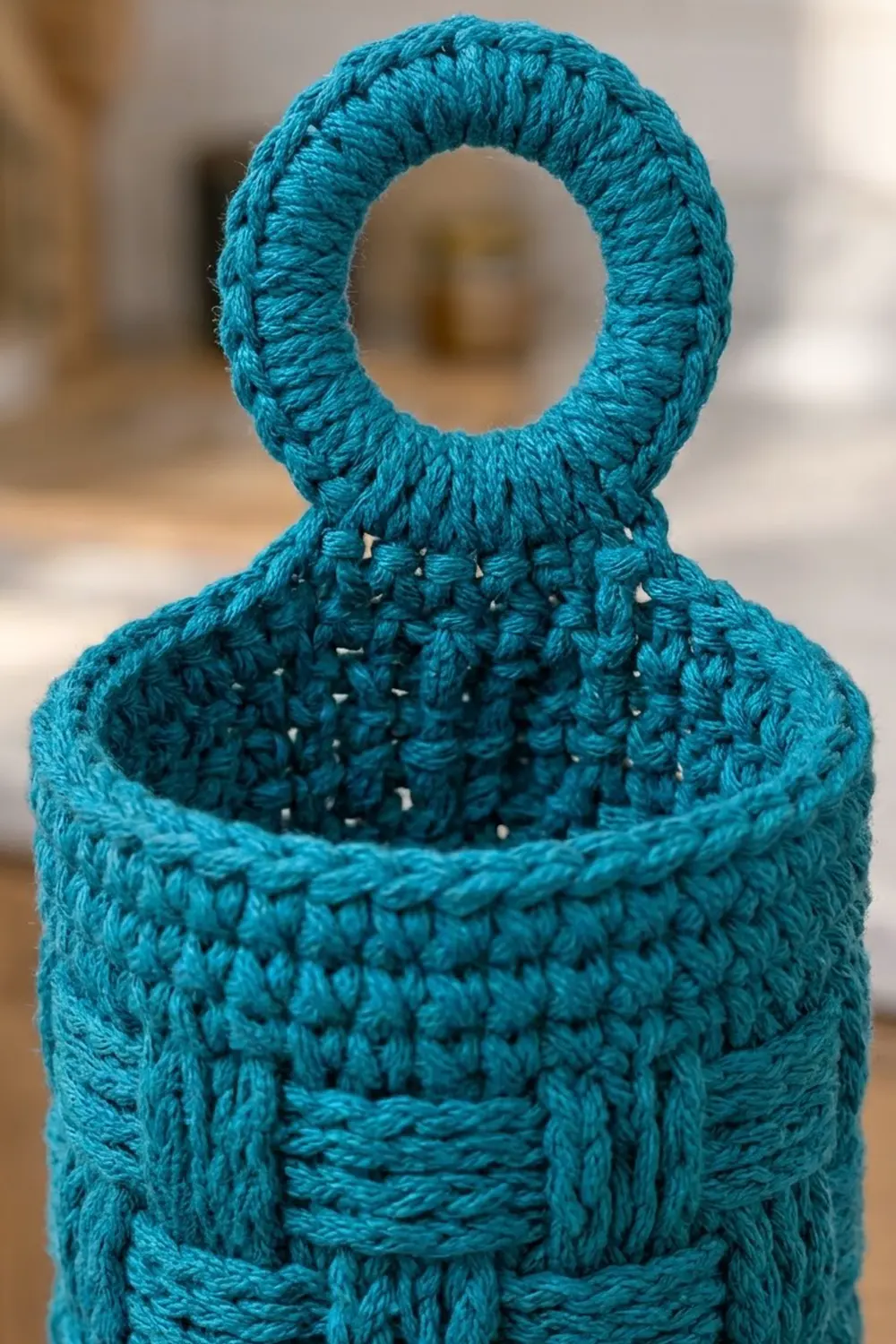 Turquoise crocheted pouch with handle loop showing detailed stitch work and open weave texture against blurred background.