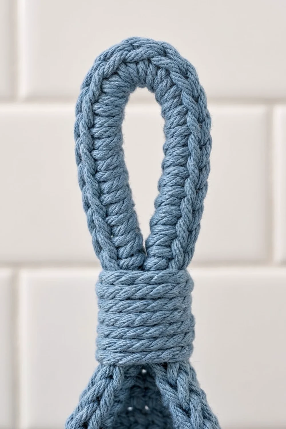 A light blue crocheted rope forms a loop with detailed cable stitching and a wrapped center binding.