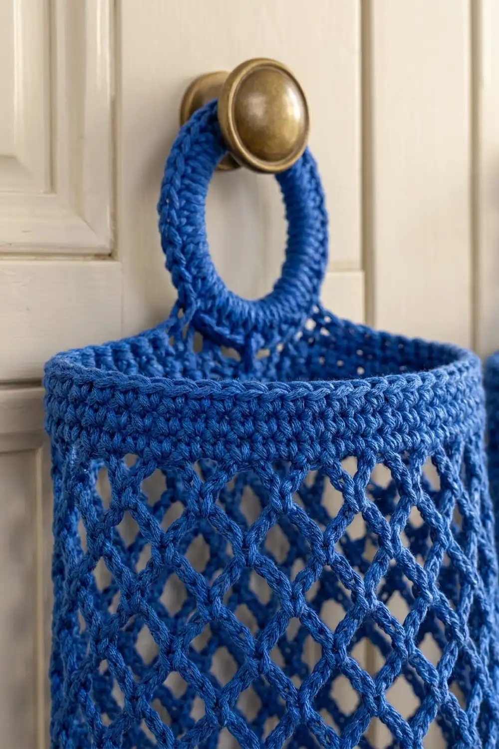 Handmade blue crochet basket with open diamond pattern and brass handle on white-paneled door.