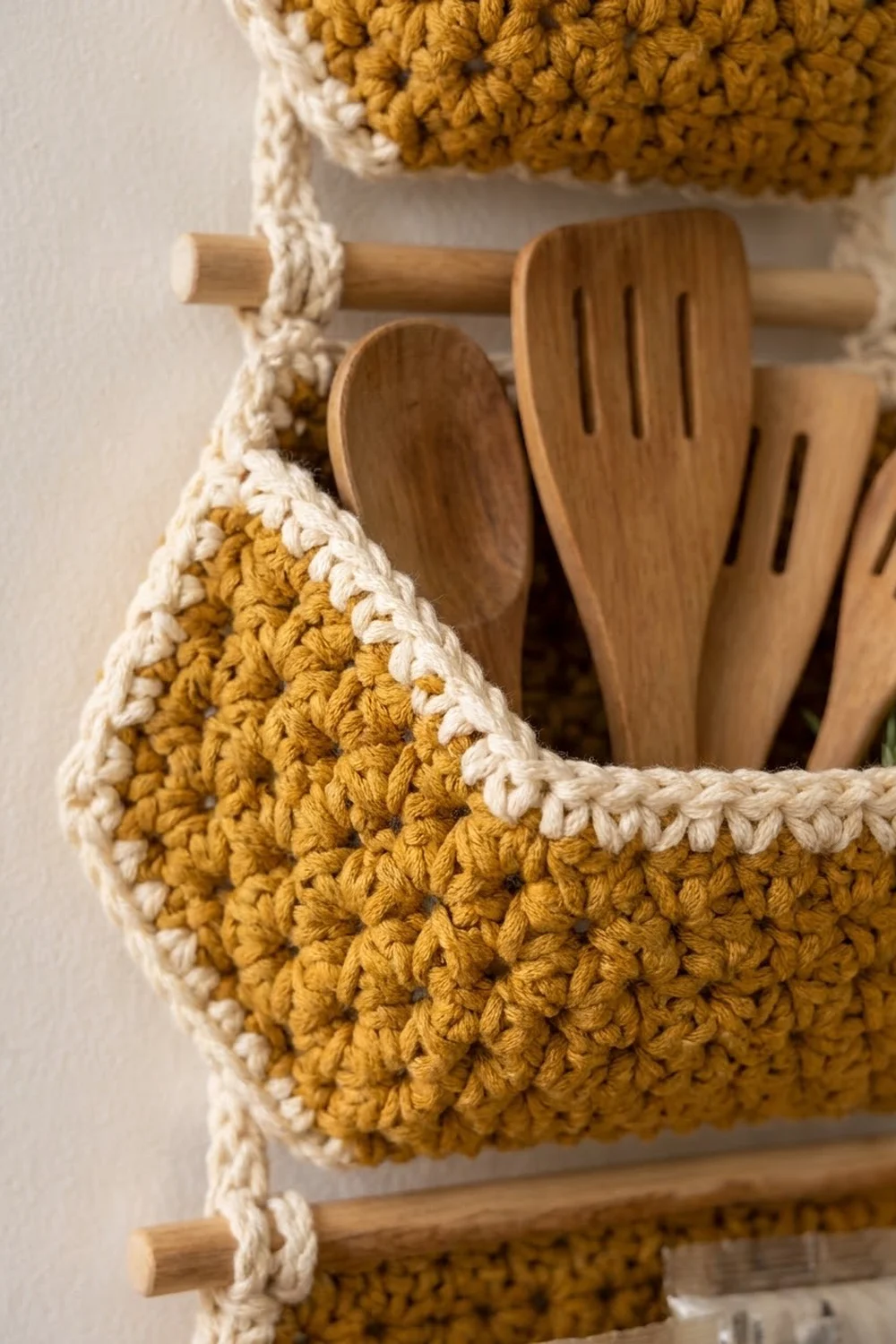 Golden-yellow crochet basket with cream trim displays wooden utensil handles inside on a neutral background.