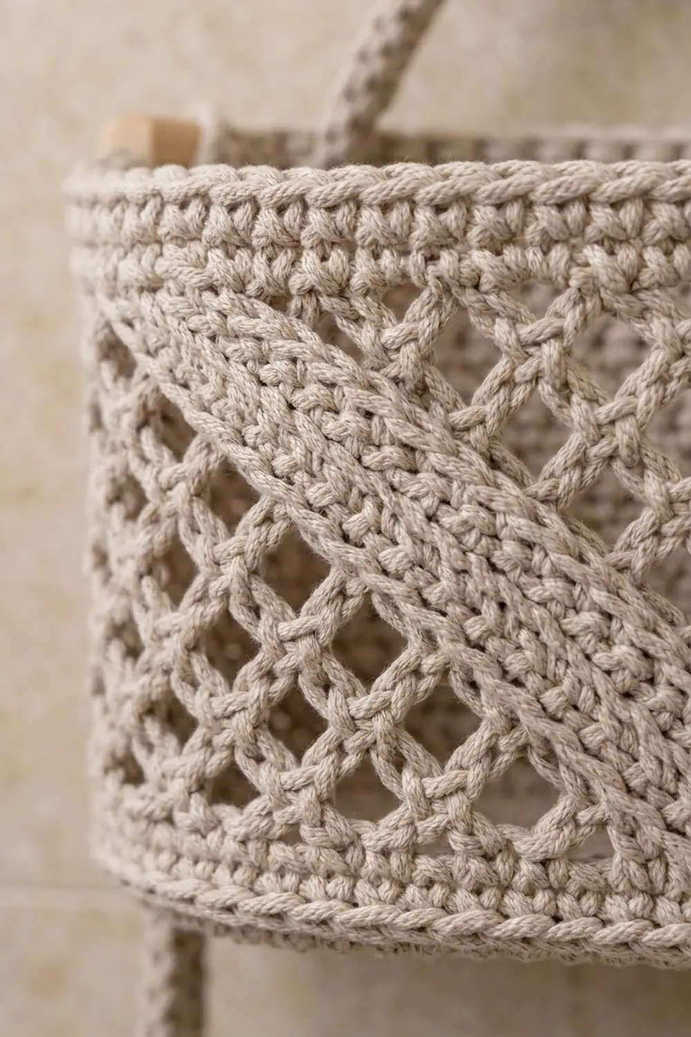 Handmade cream crochet basket with openwork diamond pattern and rope handle on blurred background.