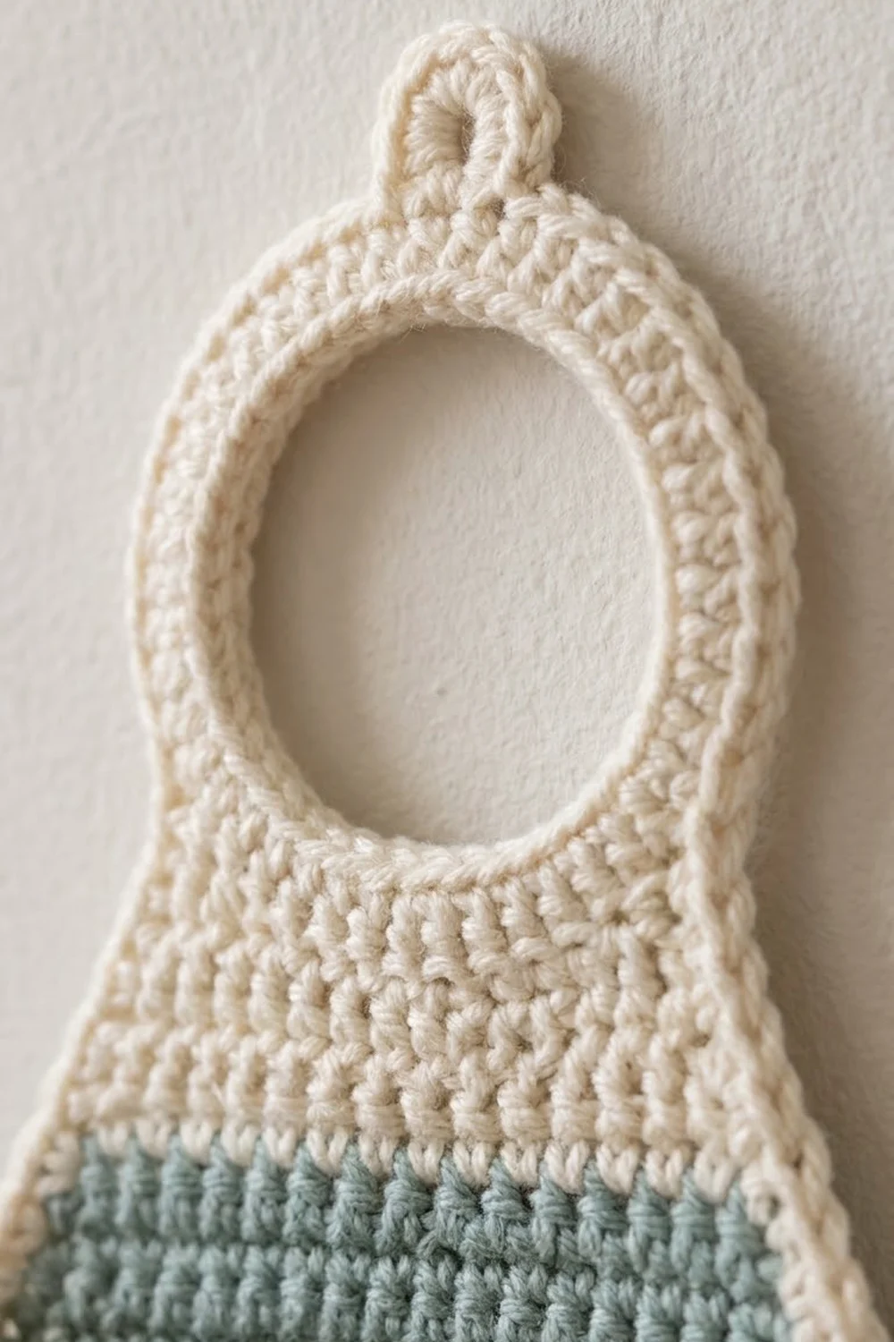 Close-up of cream-colored crocheted pouch with loop handle and sage green trim band.