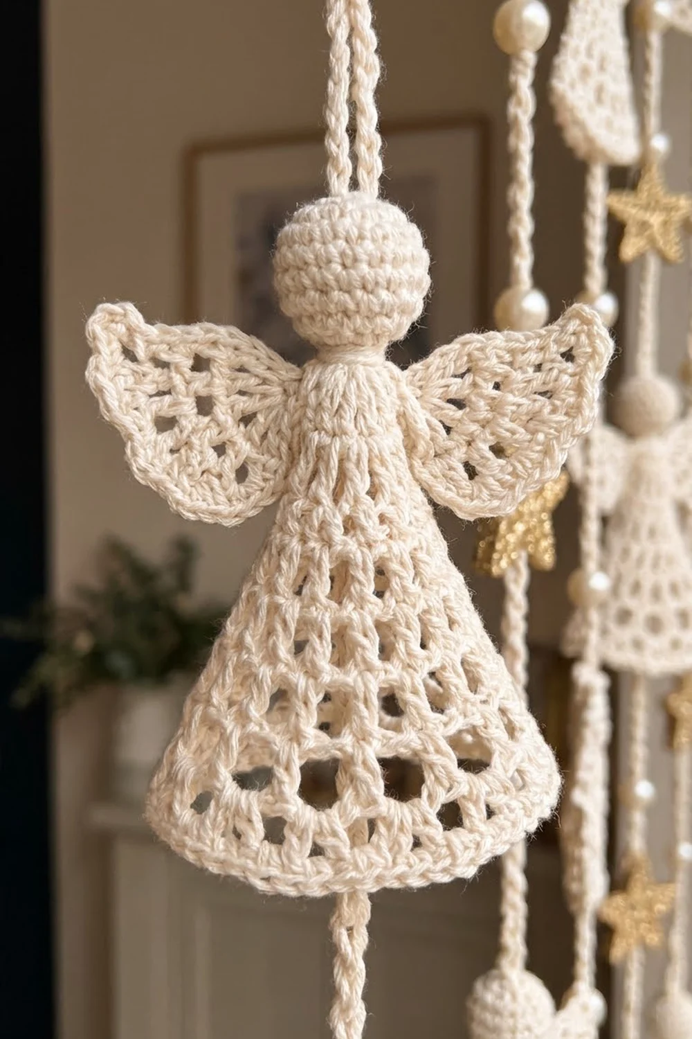 Cream crocheted angel ornament with lace-patterned wings and openwork bell dress, hanging from twisted rope.