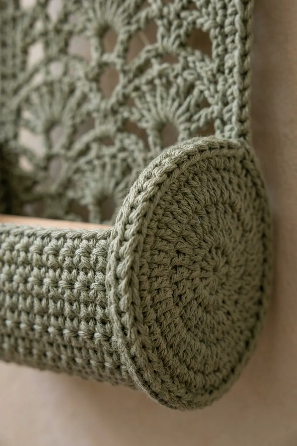 Handmade sage-green crochet cushion with detailed textured stitching on a neutral beige background.