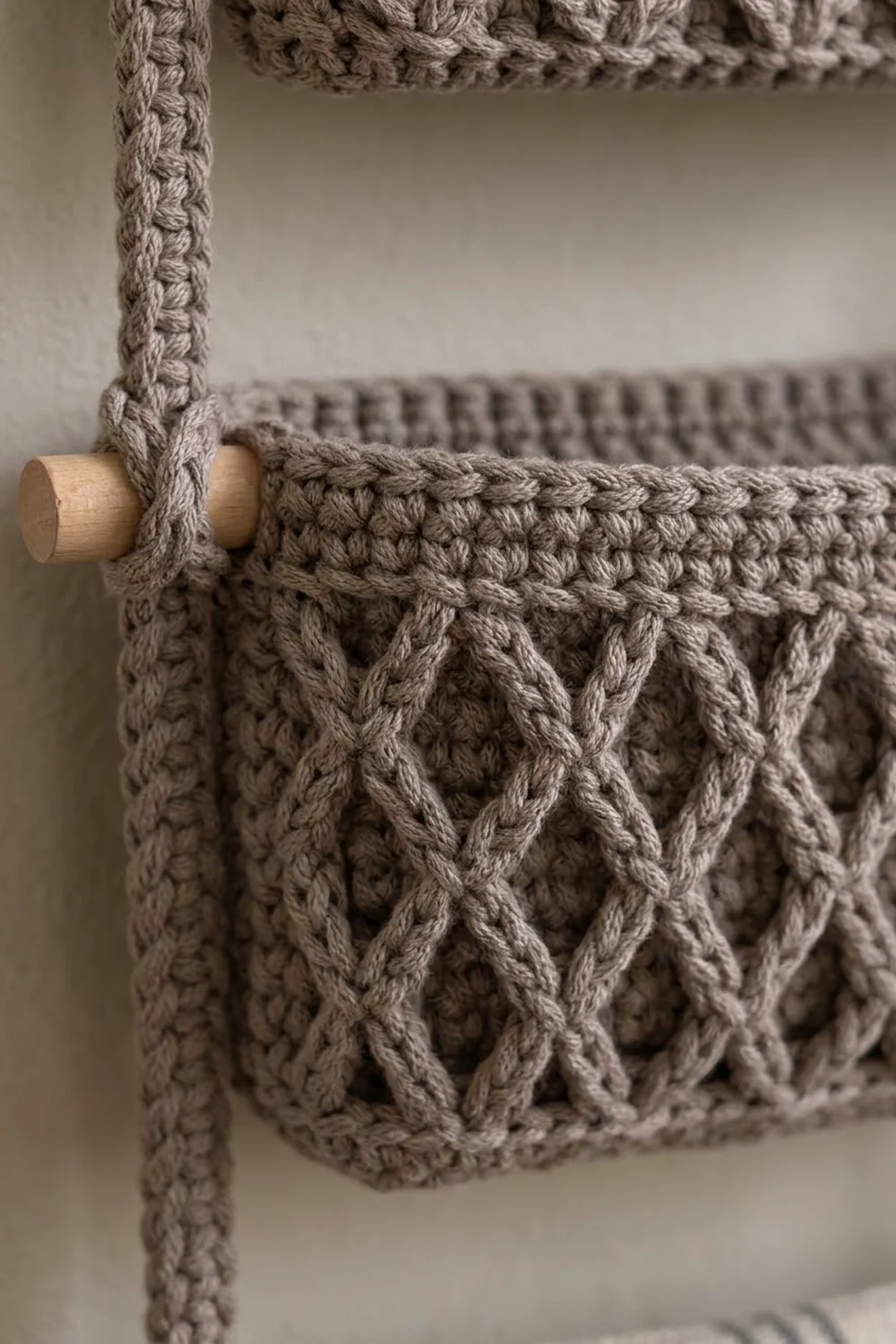 Beige crocheted fabric with textured cable pattern hanging from a light wood dowel.