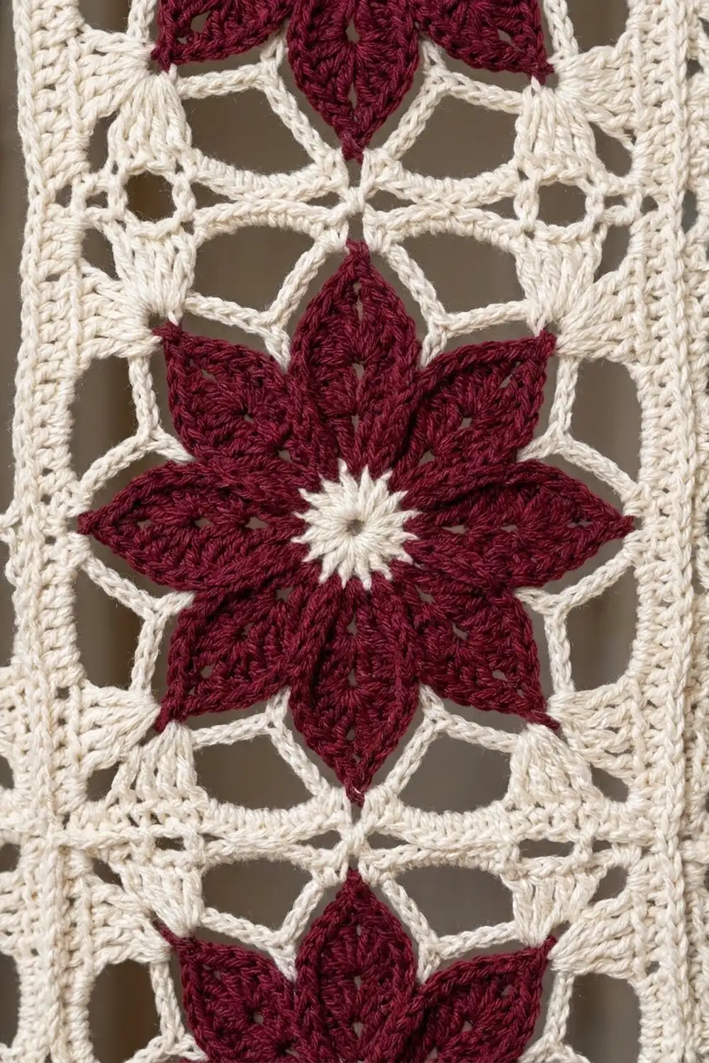 Burgundy crocheted flowers with creamy lattice openwork form a detailed repeating textile pattern.