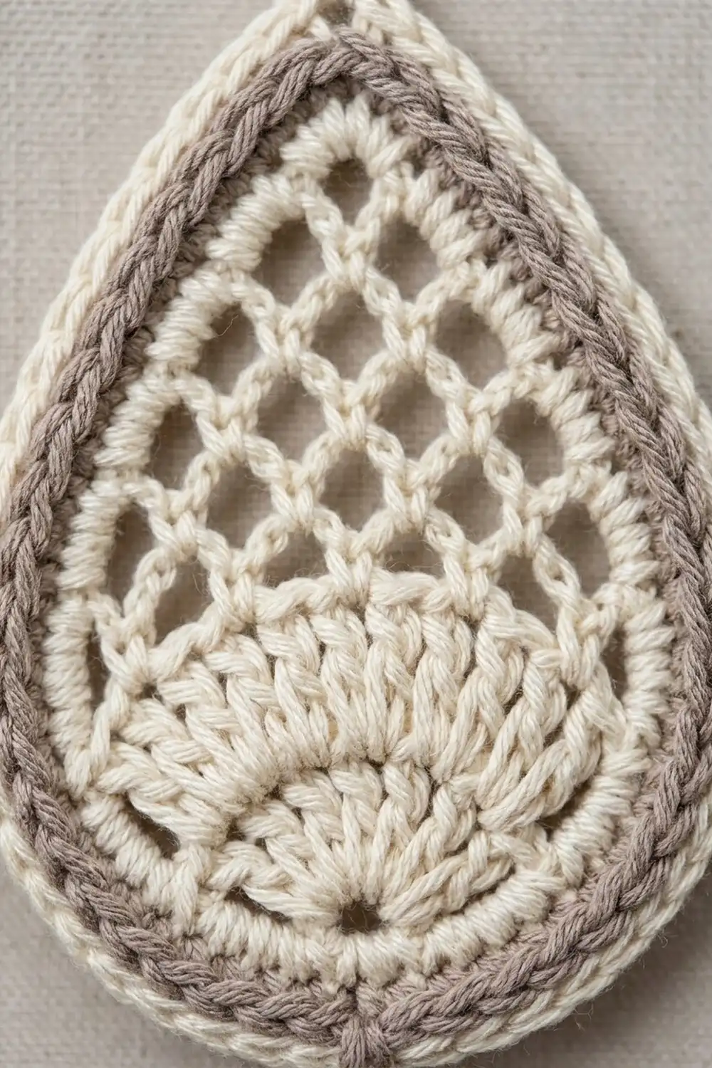 Crocheted teardrop shape with cream openwork lattice stitches and gray braided border detail on neutral background.