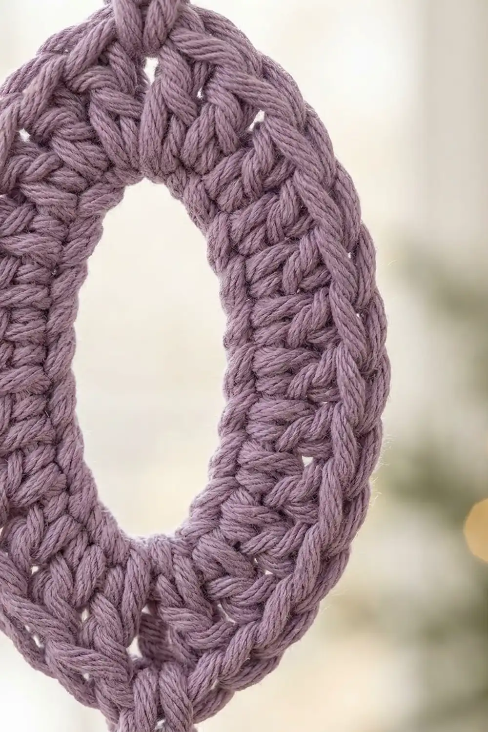 Close-up of a mauve crocheted infinity scarf showing intricate cable stitch texture and openwork pattern details.