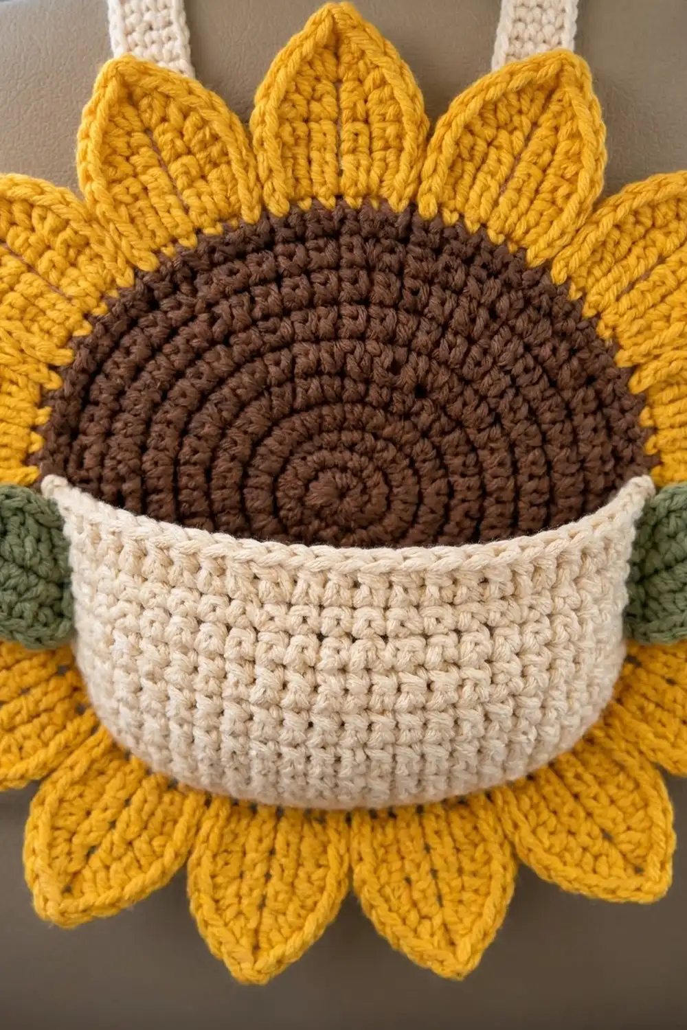 Close-up of a crocheted sunflower with bright yellow petals, dark brown seed center, and cream-colored pot.